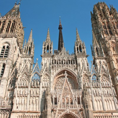a large clock tower in front of a tall building with Rouen Cathedral in the background